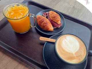 Breakfast scene with orange juice, croissants, and cappuccino on a tray