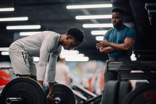 Determined young athlete lifting weights with personal trainer in gym
