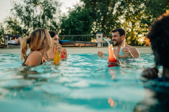 Friends enjoying colorful drinks in swimming pool during summer party