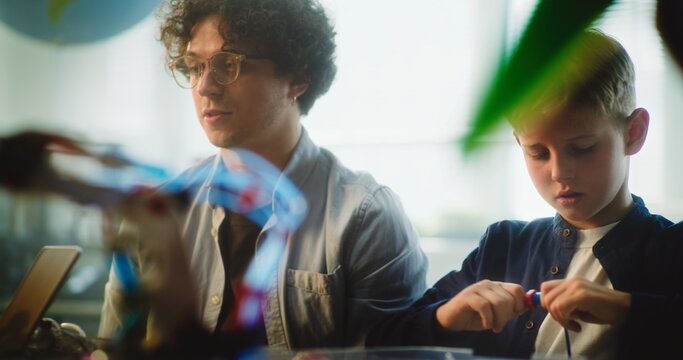 Team of Smart Kids and Young Teacher Assembling Constructor on STEM Lesson in Multiethnic Classroom. Primary School Children Exploring Robotics, Renewable Energy Models, Studying Modern Technologies. - Powered by Adobe