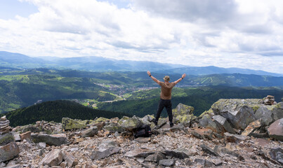 A hiker in athletic gear greets nature from the top of a rocky mountain.