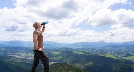 On top of a mountain, a man drinks water.