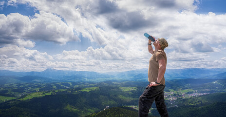 A tourist drinks water against the backdrop of a mountain landscape.