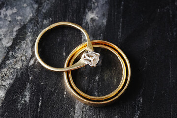 Golden wedding rings on dark marble. Elegant jewelry set with engagement ring. Marriage symbol with...
