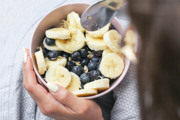Healthy oatmeal with fruits. Bowl of porridge with banana and blueberries. Hands holding breakfast....