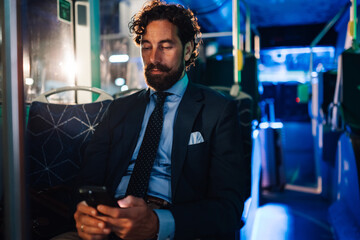 Elegant businessman using smartphone on night bus ride