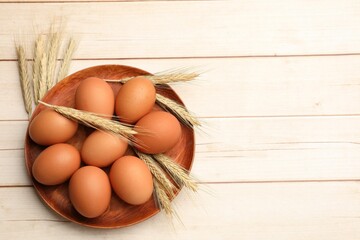 Fresh eggs and spikes on light wooden table, flat lay. Space for text