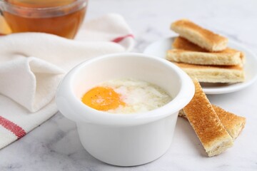 Half-boiled egg in bowl and toasted bread on white marble table, closeup. Traditional asian breakfast