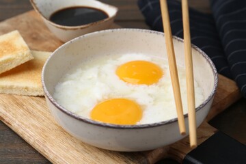 Traditional asian breakfast with half-boiled eggs in bowl, soy sauce, bread and chopsticks on wooden table, closeup