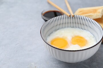 Traditional asian breakfast with half-boiled eggs in bowl, soy sauce, bread and chopsticks on grey table, closeup. Space for text