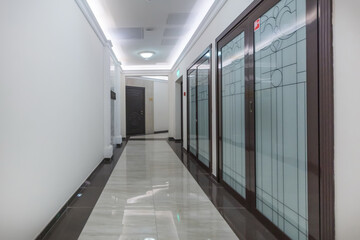 A long, bright corridor. The floor is decorated with white and dark tiles. Double-leaf 
glass doors...