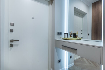 Entrance hall in the apartment with a white entrance door. A small table near the mirrored wall with a backlight.