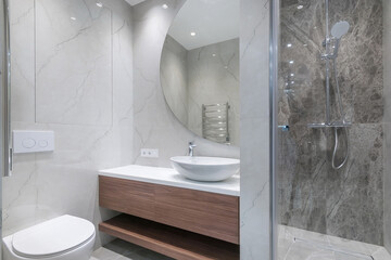 Modern bathroom design, decorated with white and gray marble tiles. A large round mirror over the...
