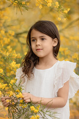 Spring and summer portrait of little girl in white dress with yellow blooming flowers in desert