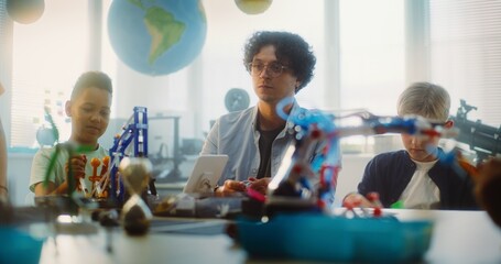 Team of Smart Kids and Young Teacher Assembling Constructor on STEM Lesson in Multiethnic Classroom. Primary School Children Exploring Robotics, Renewable Energy Models, Studying Modern Technologies.