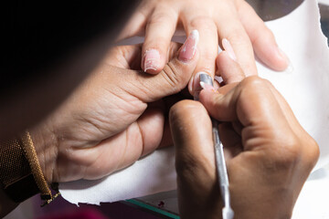 Fototapeta premium An unrecognizable woman's hands cleaning a client's nail inside a beauty salon in Neiva, Huila, Colombia. Concept of work and professional services