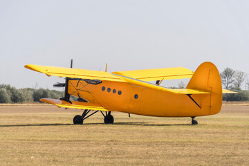 A parked yellow biplane old Soviet-made transport plane on a grassy airfield
