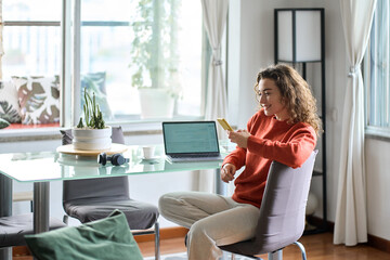Young pretty woman holding smartphone using cellphone modern technology. Smiling lady looking at mobile phone while remote working or e learning from home sitting at table with laptop computer.