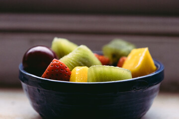 Blue bowl with fruit such as kiwi, strawberry, mango and grapes. Detailed close-up shot. Healthy nutrition concept