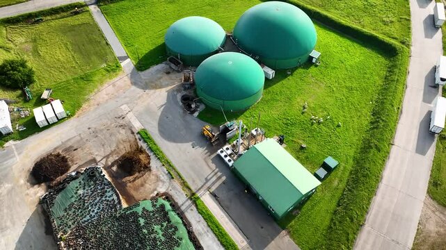 Aerial footage of green-roofed biogas digester facility, combined heat and power station, silage storage and sheep grazing on the pasture. Sustainable energy production