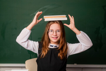 Fototapeta na wymiar Back to school. Child holding stack of books with mortar board on blackboard. School girl. School child. Portrait of elementary pupil. Happy schoolgirl. Schoolkid or preschooler.