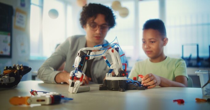 Science and Technology Lesson: Elementary School Student Studying Model of Robotic Arm. Young Teacher Educating Smart African American Boy in Modern Classroom. Interactive Learning and STEM Education.