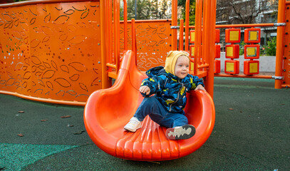 A young child wearing a yellow hat on a red slide.