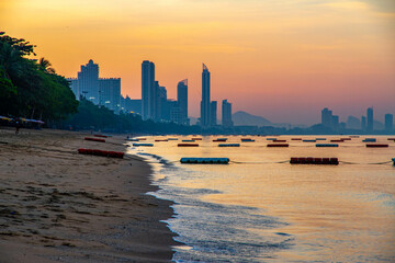 Dawn view of Jomtien Beach, Pattaya, Thailand. City skyline and distant hills silhouetted against a...