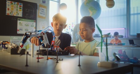 Team of Multiethnic Talented Boys Sitting at Table, Studying Robotic Arm Model. Primary School Children During Science and Technology Lesson in Modern Classroom. Interactive Learning, STEM Education. © Framestock