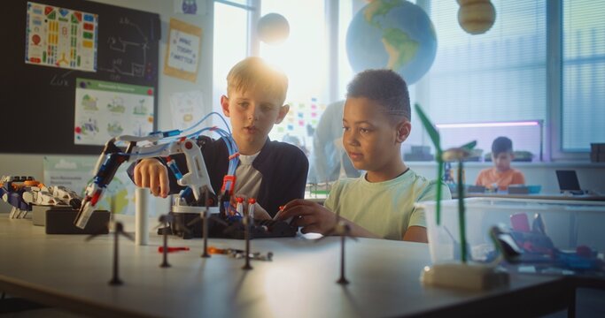 Team of Multiethnic Talented Boys Sitting at Table, Studying Robotic Arm Model. Primary School Children During Science and Technology Lesson in Modern Classroom. Interactive Learning, STEM Education. - Powered by Adobe