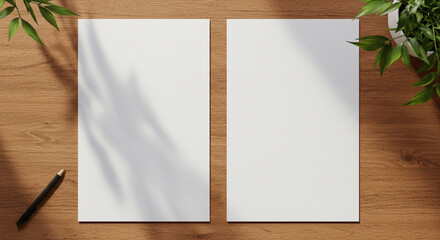 Two blank white papers on a wooden desk with a pen and a plant casting shadows from above light source