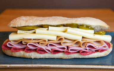 Sandwich with salami, ham, turkey, cheese and pickles on a plate