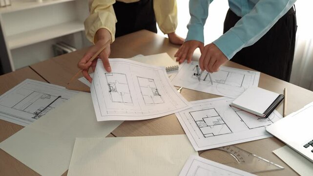 Architect and safety engineer discussion about building blueprint displaying on laptop on table with architectural document and wooden block scatter around at modern office. Closeup. Delineation.