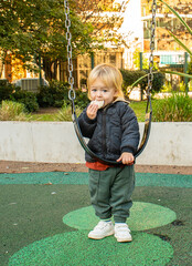 A little boy is eating a snack while sitting on a swing