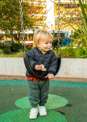 A little boy is eating a snack while sitting on a swing