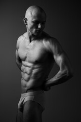 Fototapeta premium Black and white image of a muscular man showcasing his physique with a confident pose, emphasizing strength and determination in a minimalist setting.