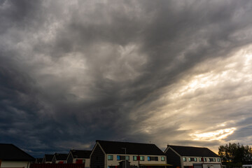 Dark storm clouds forming above modern suburban houses at sunset with dramatic sky and contrast...