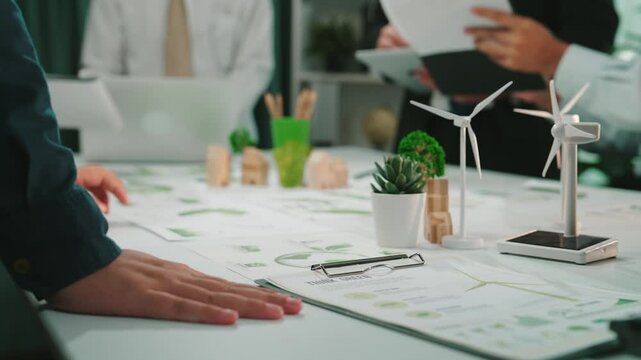 A collaborative meeting scene showcasing diverse professionals focusing on sustainable energy projects. Hands interact with charts and data in a modern office space. SACTR