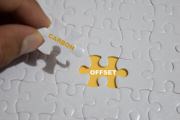 Hand holding piece of jigsaw puzzle with word carbon and offset.