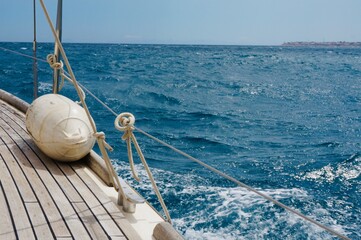 Sailboat navigating through vibrant blue waters, showcasing the wooden deck and buoy, capturing the essence of maritime adventure and tranquility