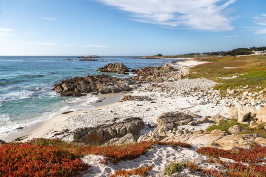 Scenic view of rocky coastline and sandy beach in 17 Mile Drive, Del Monte Forest, California, USA. Waves crash against the rocks, creating a peaceful and serene atmosphere.
