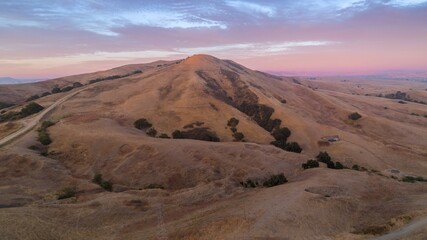 Aerial view of San Juan Bautista, California, USA, at sunset. The golden hills and pink sky create a serene landscape.
