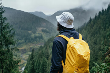 Person with a yellow backpack views a misty mountain valley.
