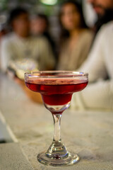 Red Craft Cocktail in Coupe Glass on Bar Counter with People in Background - Nightlife and Happy Hour Scene