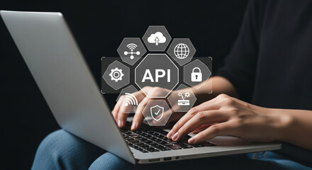 Person typing on laptop with api graphic overlay showing cloud and security icons on black background