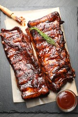 Tasty roasted pork ribs served with rosemary and sauce on black table, top view © New Africa
