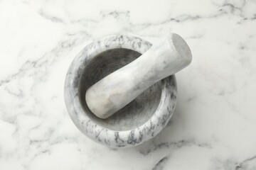 Mortar and pestle on white marble table, top view