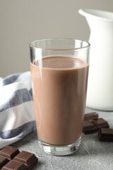 Tasty chocolate milk in glass and pieces on grey table, closeup