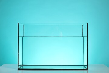 Glass aquarium with water on white table against turquoise background