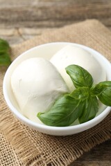 Tasty mozzarella cheese and basil on wooden table, closeup